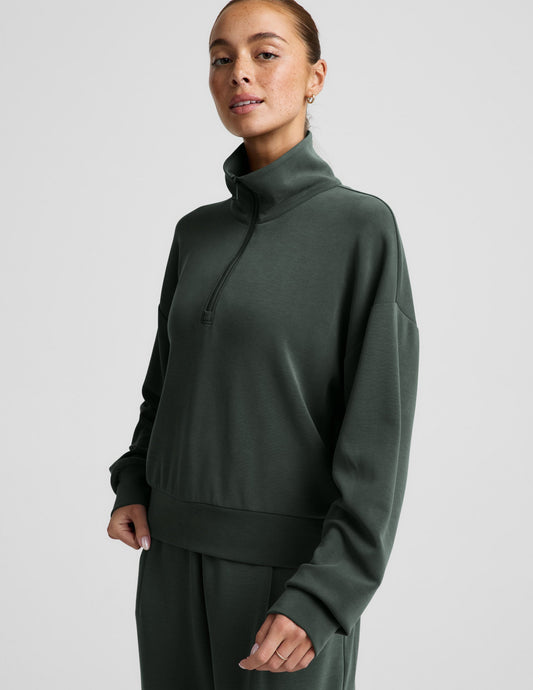 Woman wearing a green quarter zip sweatshirt and green wide leg pants against a plain background.