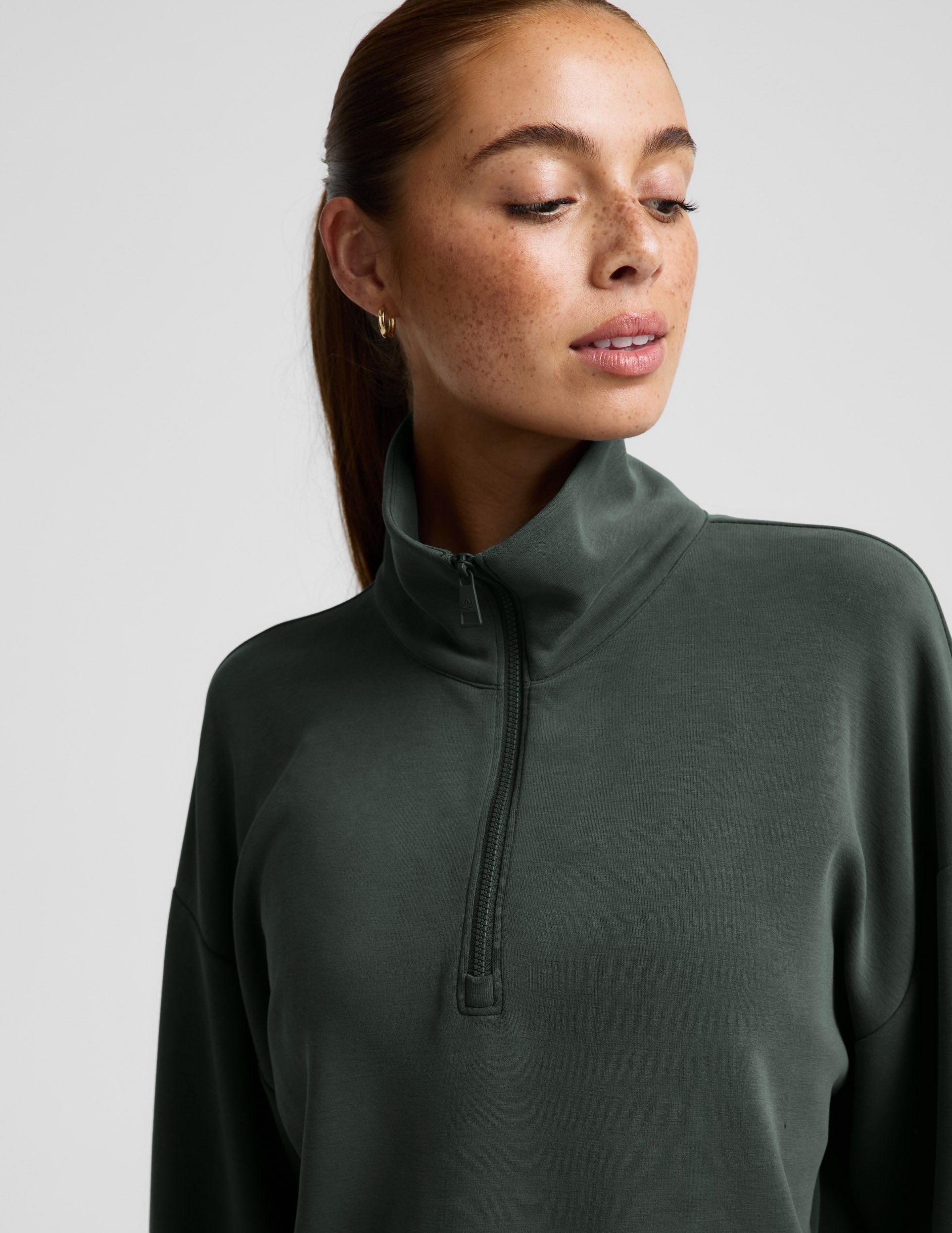 Woman wearing a green quarter zip sweatshirt and green wide leg pants against a plain background.