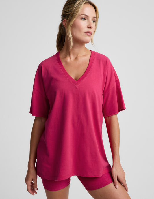 Woman wearing a red v-neck oversized cotton t-shirt and biker shorts against a plain background.