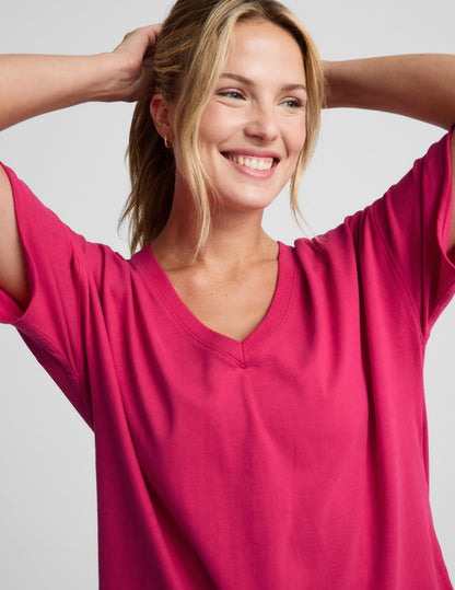 Woman wearing a red v-neck oversized cotton t-shirt and biker shorts against a plain background.