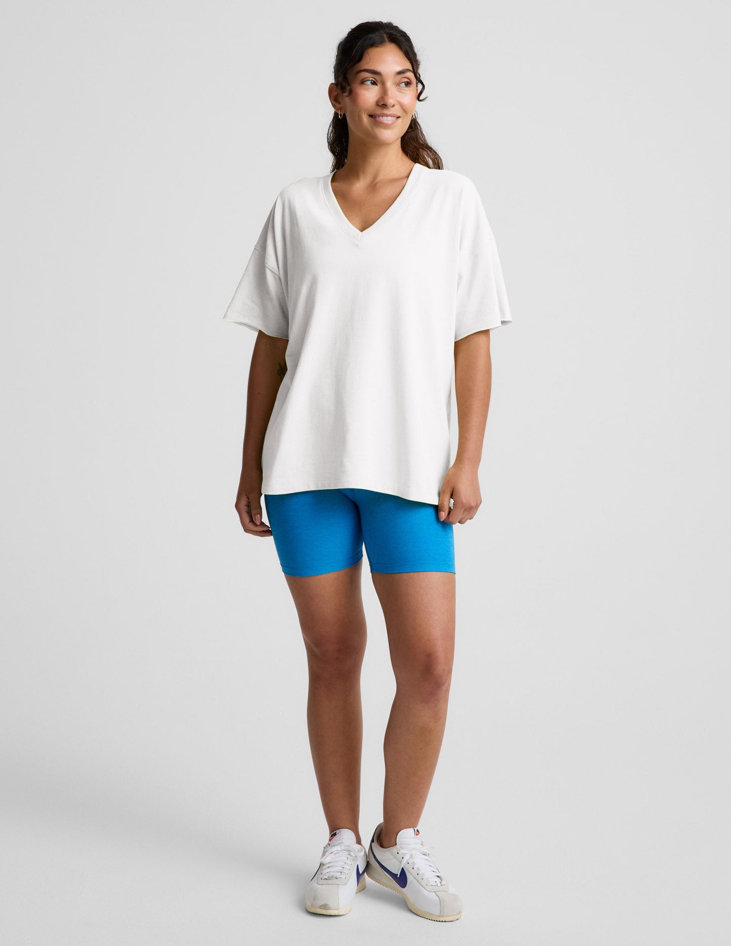 Woman wearing a white v-neck oversized t-shirt and blue biker shorts against a plain background.