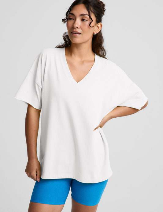 Woman wearing a white v-neck oversized t-shirt and blue biker shorts against a plain background.
