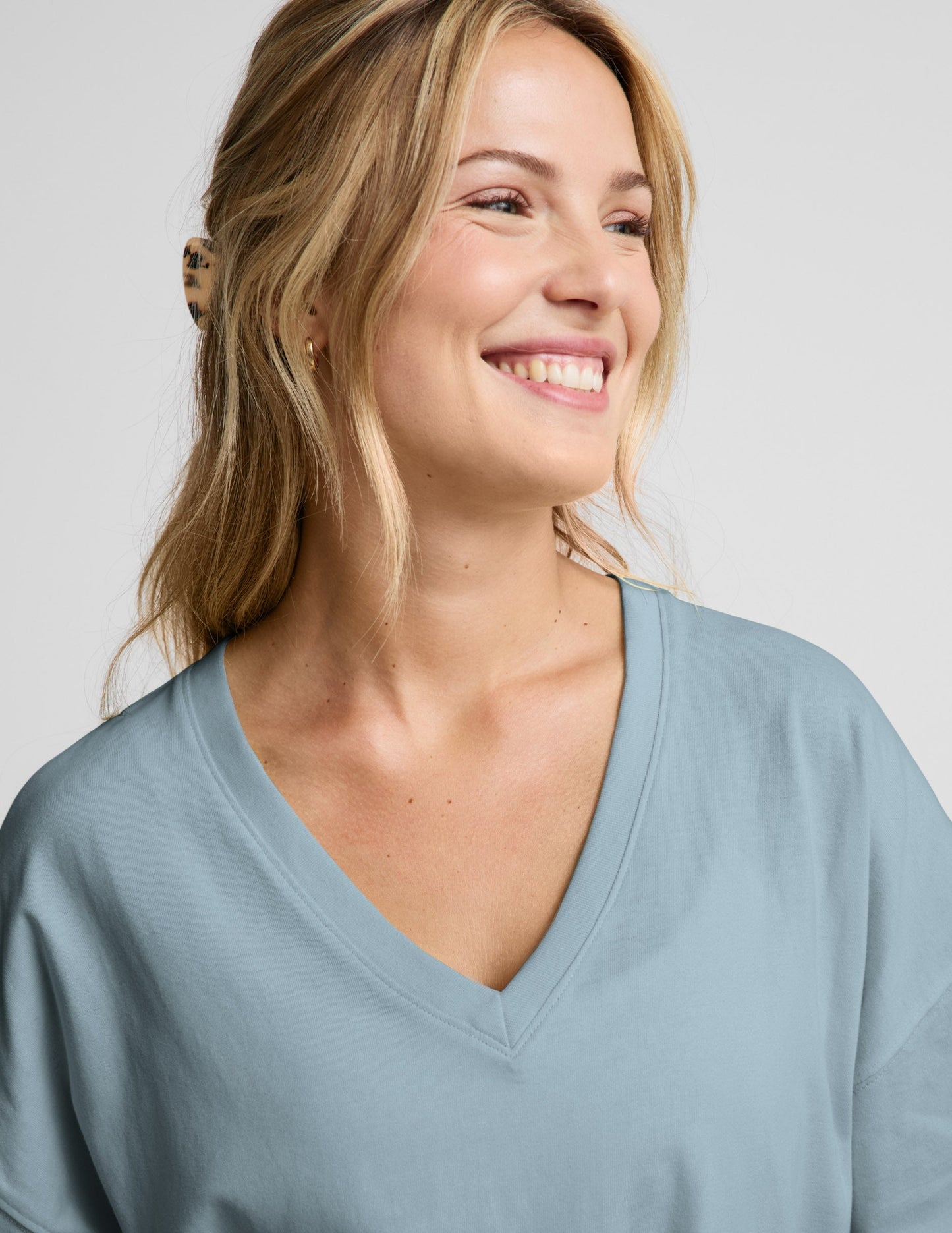 Woman wearing a blue v-neck oversized t-shirt and blue shorts against a plain background.