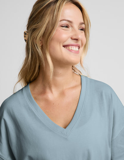 Woman wearing a blue v-neck oversized t-shirt and blue shorts against a plain background.