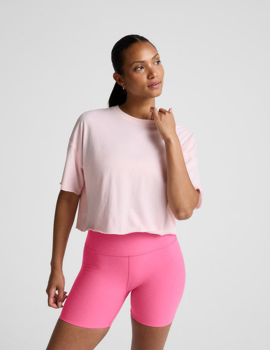 Woman wearing a light pink cropped t-shirt and pink biker shorts against a plain background.
