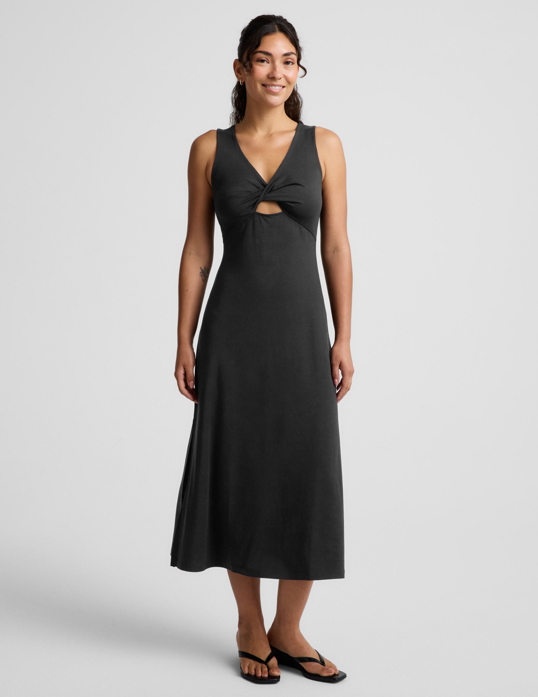 Woman wearing a black sleeveless midi dress with a cutout design on a light gray background.
