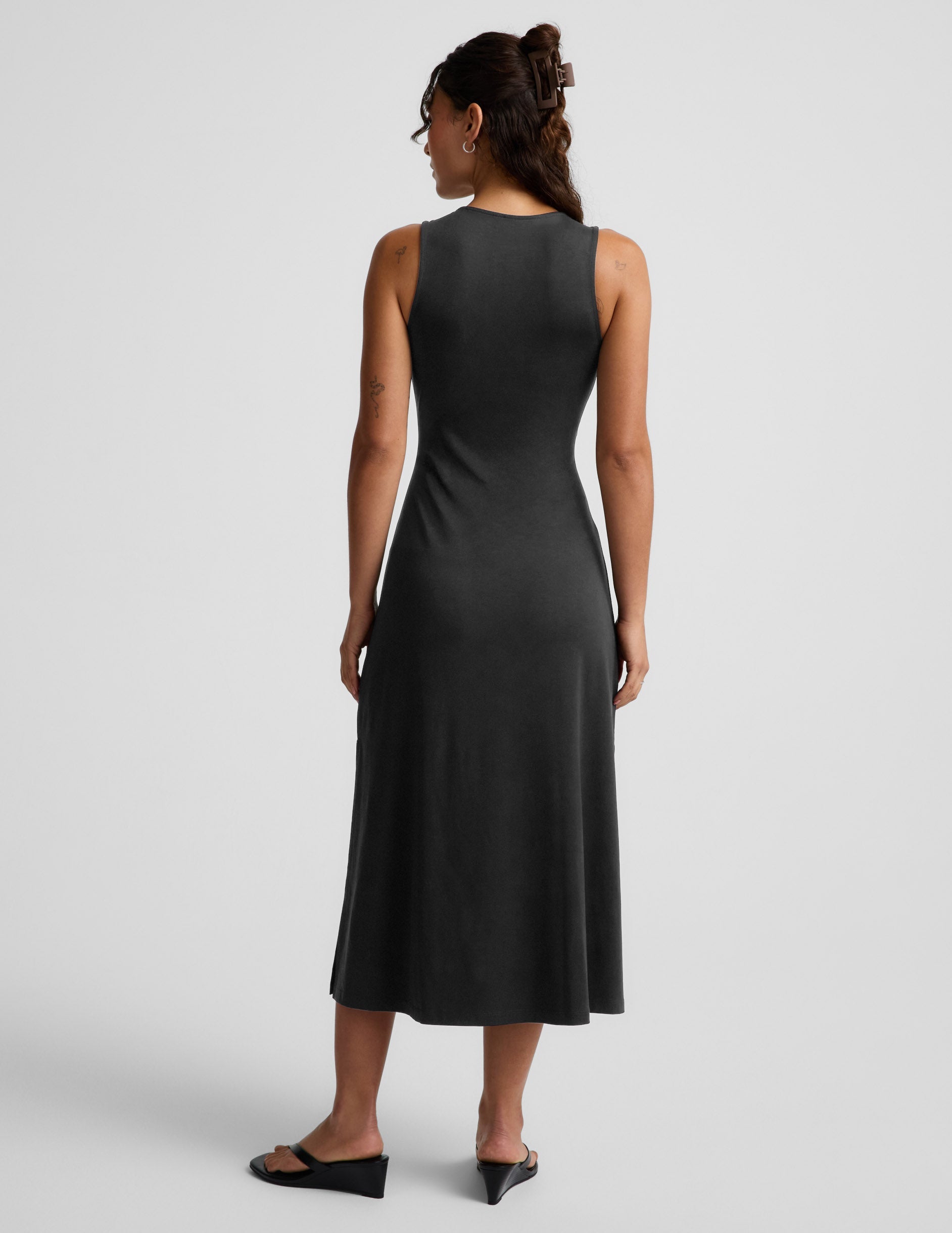 Woman wearing a black sleeveless midi dress with a cutout design on a light gray background.