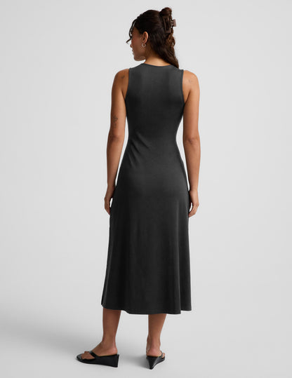 Woman wearing a black sleeveless midi dress with a cutout design on a light gray background.
