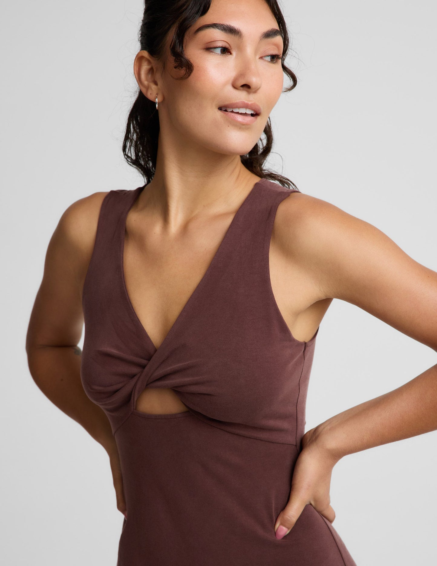 Woman wearing a brown sleeveless dress with a front center cutover on a light gray background.