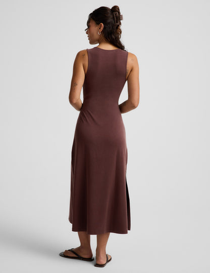 Woman wearing a brown sleeveless dress with a front center cutover on a light gray background.