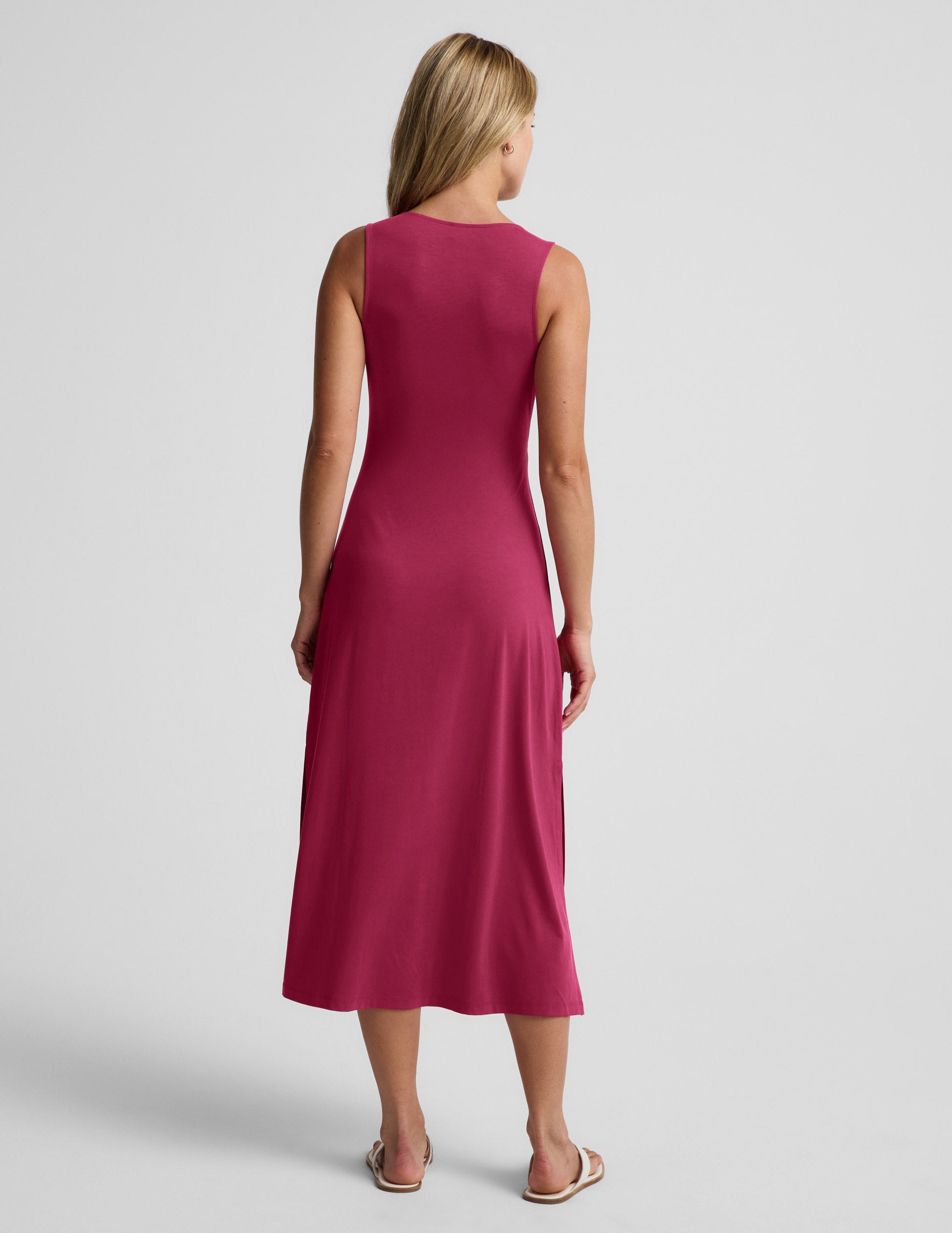 Woman wearing a red midi tank dress with a front center cutover against a light gray background.