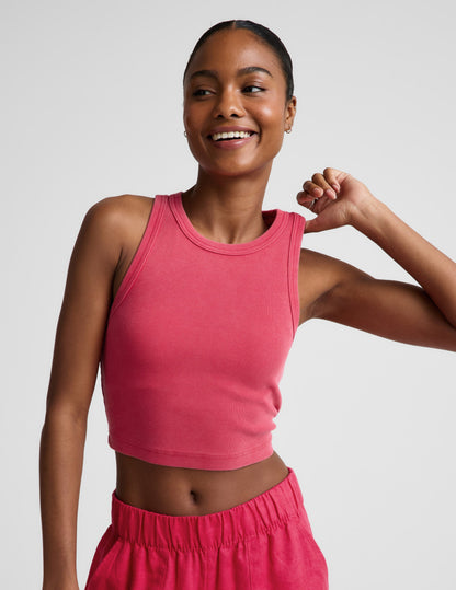 Woman wearing a red ribbed cropped tank top and red linen pants against a plain background.