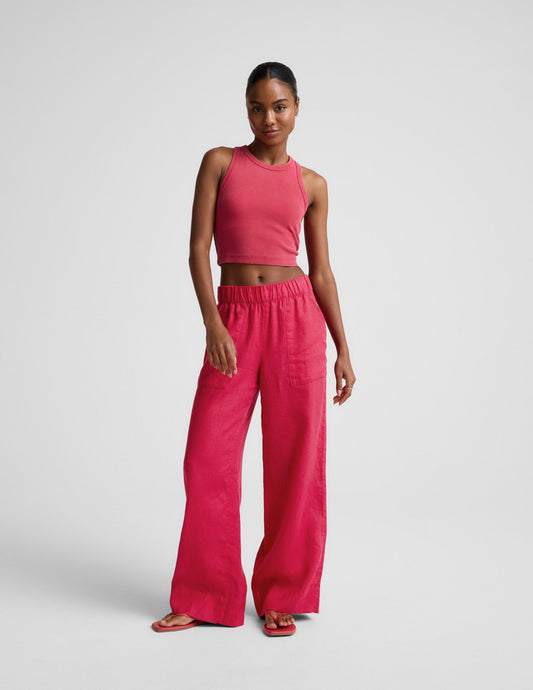 Woman wearing a red ribbed cropped tank top and red linen pants against a plain background.
