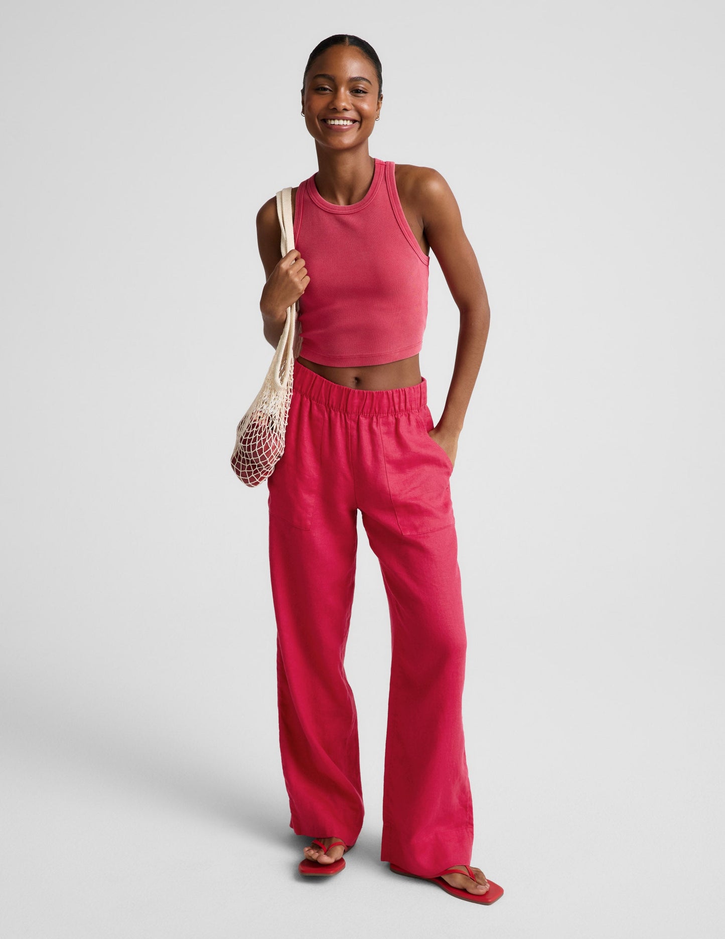 Woman wearing a red ribbed cropped tank top and red linen pants against a plain background.
