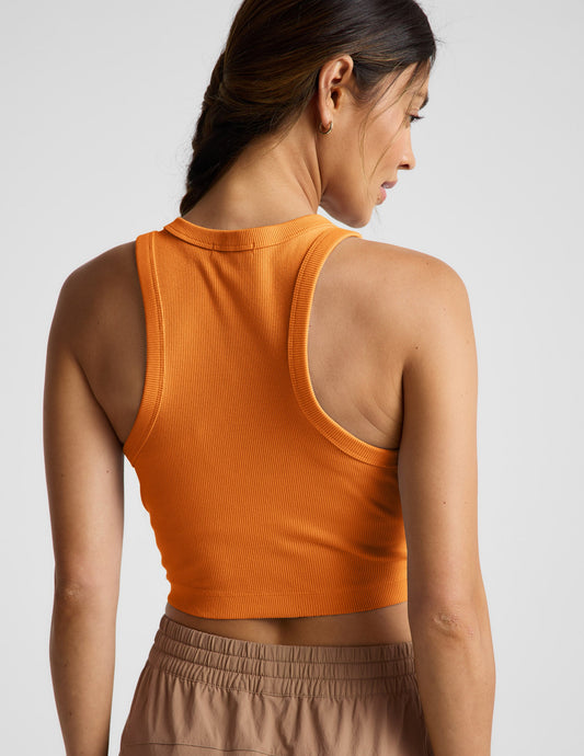 Woman wearing an orange ribbed cropped tank top and khaki cargo style pants against a plain background.
