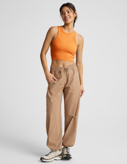 Woman wearing an orange ribbed cropped tank top and khaki cargo style pants against a plain background.