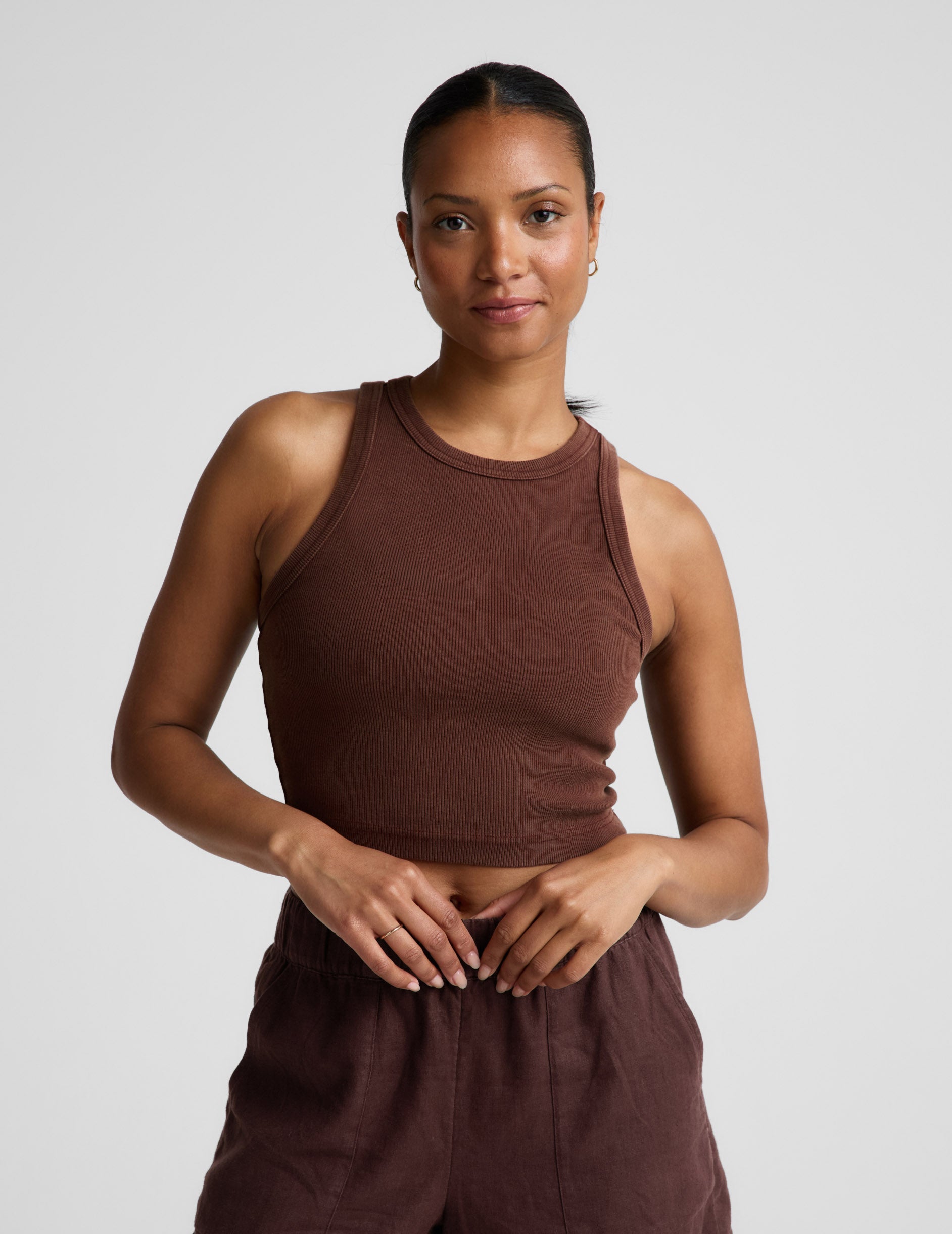 Woman wearing a brown ribbed cropped tank and brown linen shorts against a plain background.