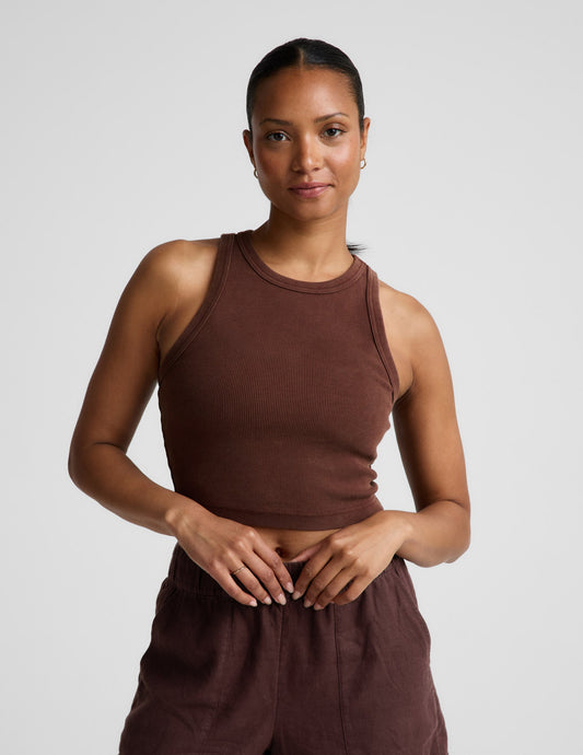 Woman wearing a brown ribbed cropped tank and brown linen shorts against a plain background.