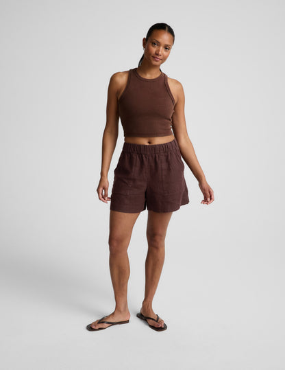 Woman wearing a brown ribbed cropped tank and brown linen shorts against a plain background.
