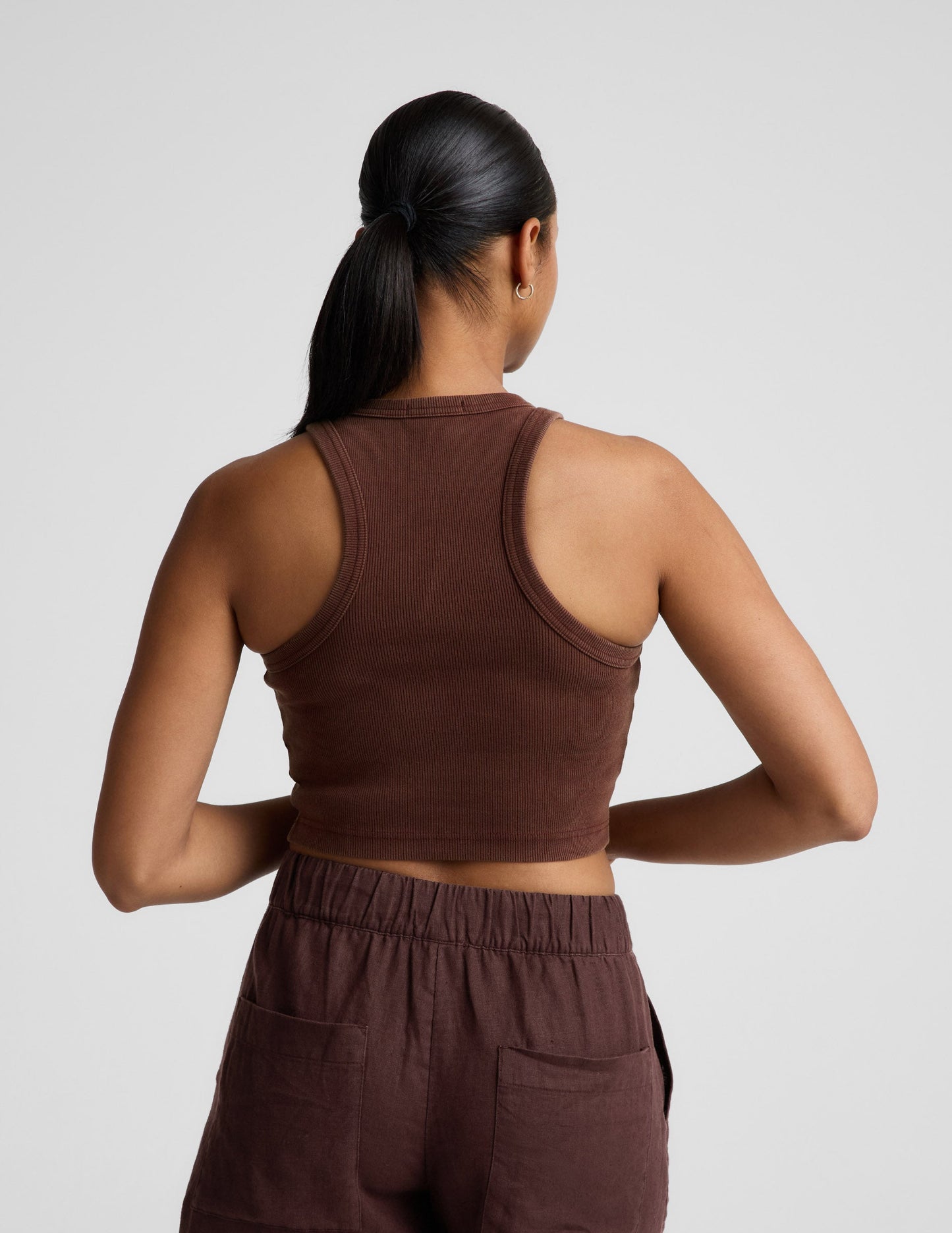 Woman wearing a brown ribbed cropped tank and brown linen shorts against a plain background.