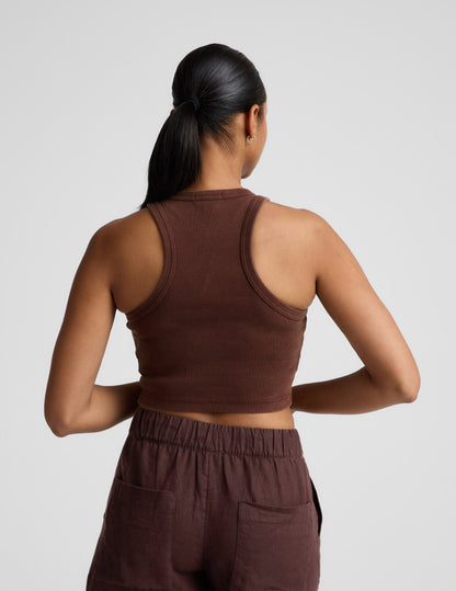 Woman wearing a brown ribbed cropped tank and brown linen shorts against a plain background.