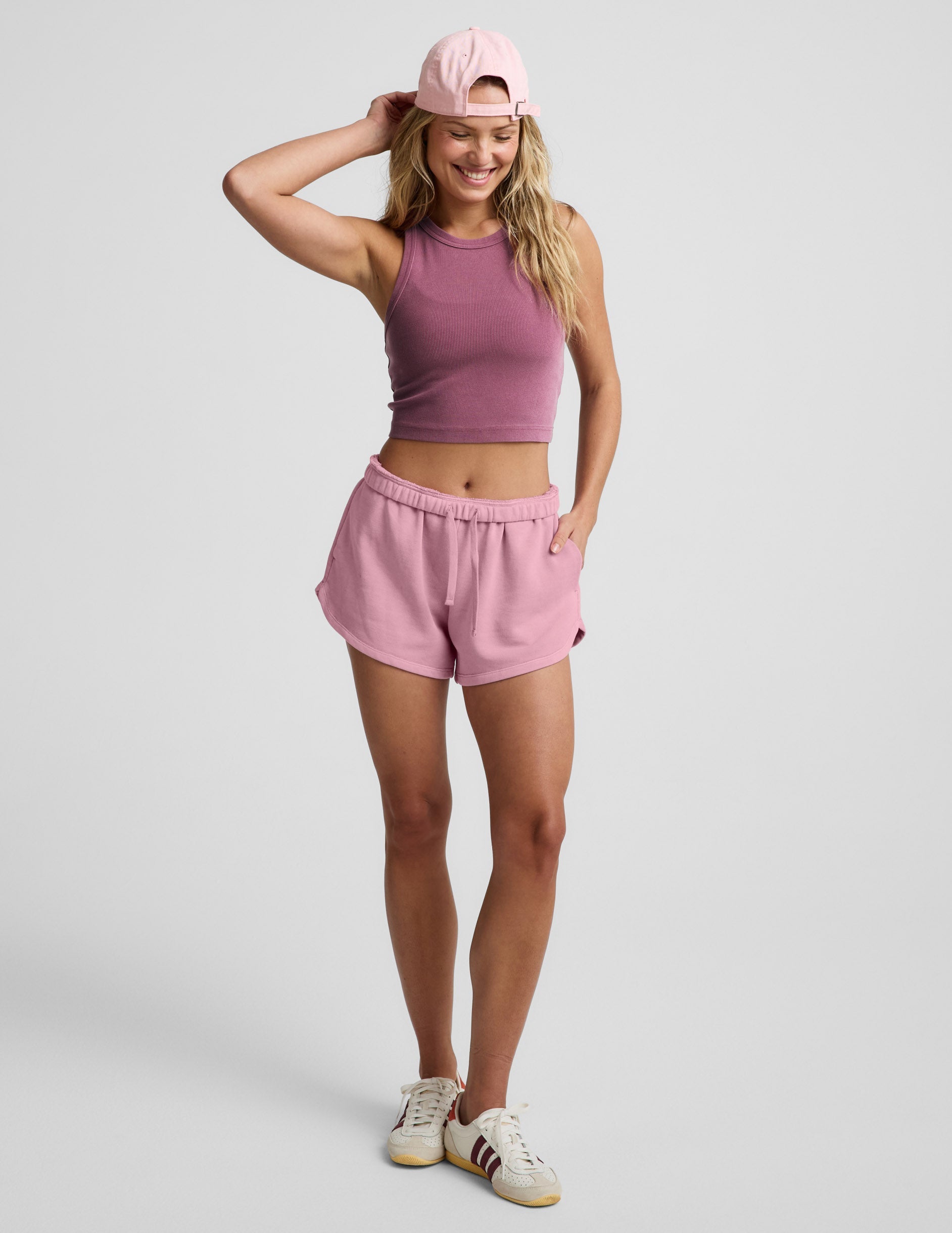 Woman wearing a purple ribbed cropped tank and pink fleece shorts against a plain background.