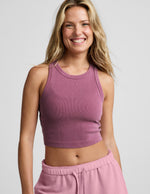 Woman wearing a purple ribbed cropped tank and pink fleece shorts against a plain background.