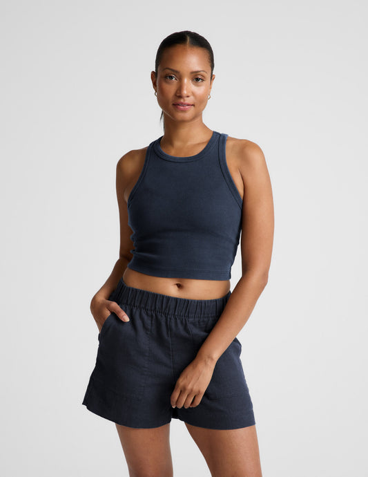 Woman wearing a navy ribbed tank top and linen shorts against a plain background.