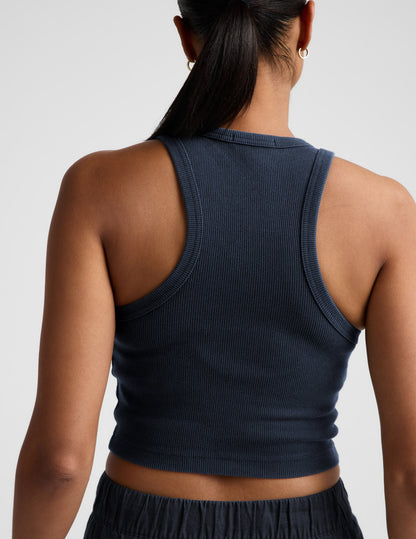 Woman wearing a navy ribbed tank top and linen shorts against a plain background.