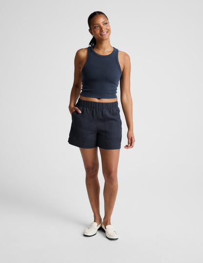 Woman wearing a navy ribbed tank top and linen shorts against a plain background.