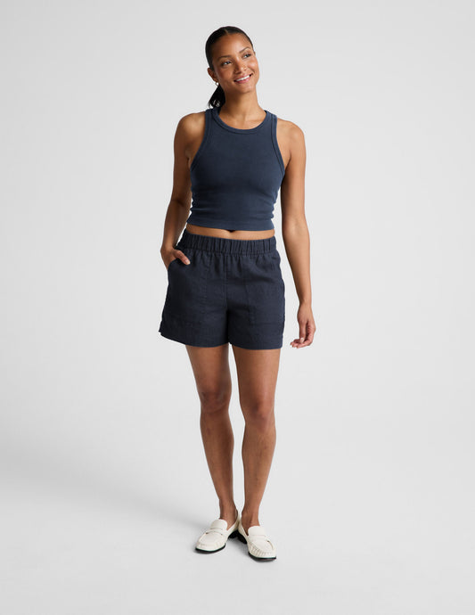 Woman wearing a navy ribbed tank top and linen shorts against a plain background.
