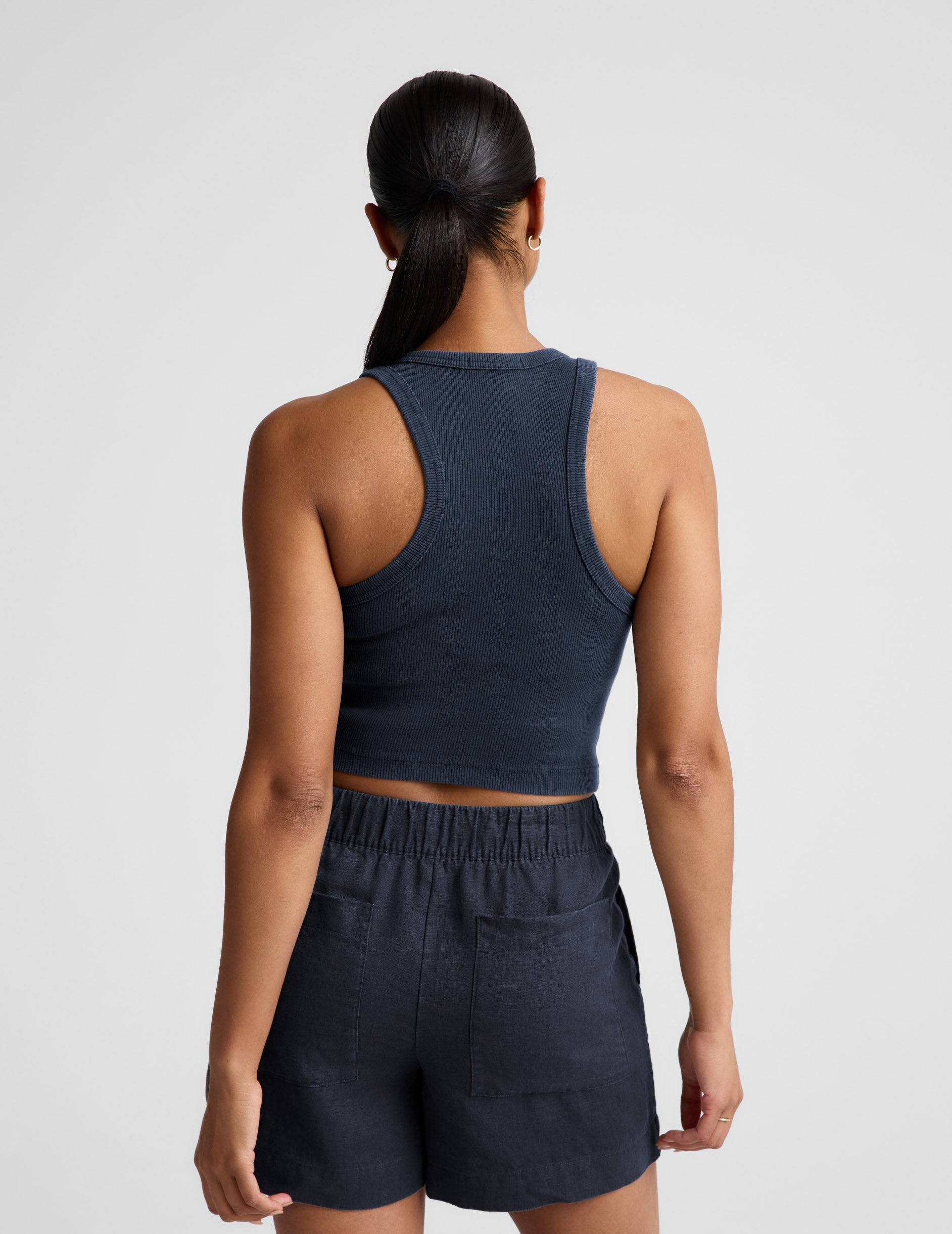 Woman wearing a navy ribbed tank top and linen shorts against a plain background.