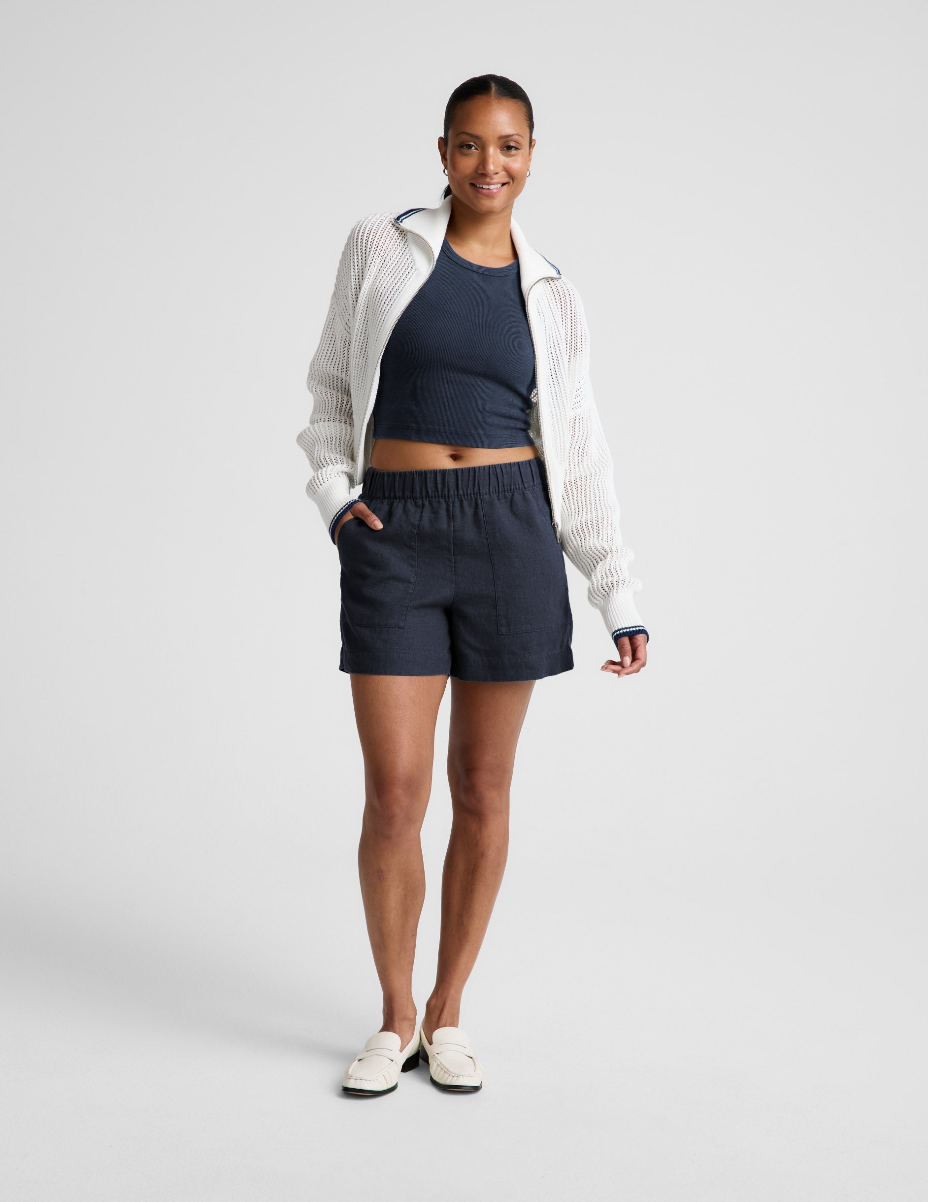Woman wearing a navy ribbed tank top and linen shorts against a plain background.