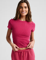 Woman wearing a red ribbed cropped t-shirt and red shorts against a plain background.
