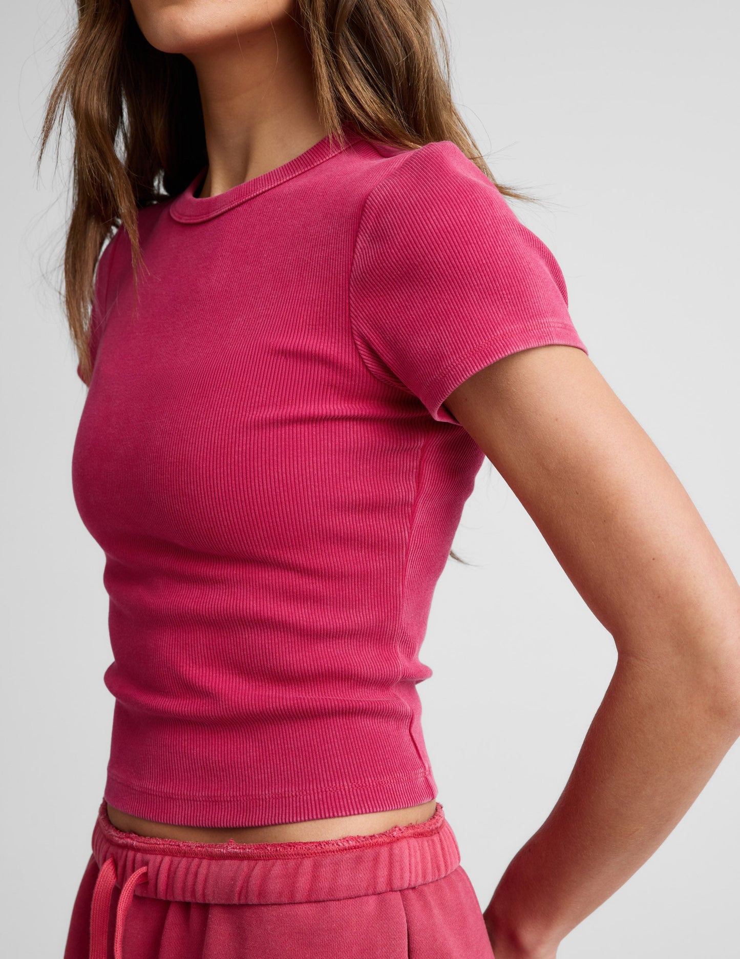 Woman wearing a red ribbed cropped t-shirt and red shorts against a plain background.