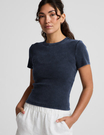 Woman wearing a navy blue ribbed t-shirt and white linen shorts against a plain background.