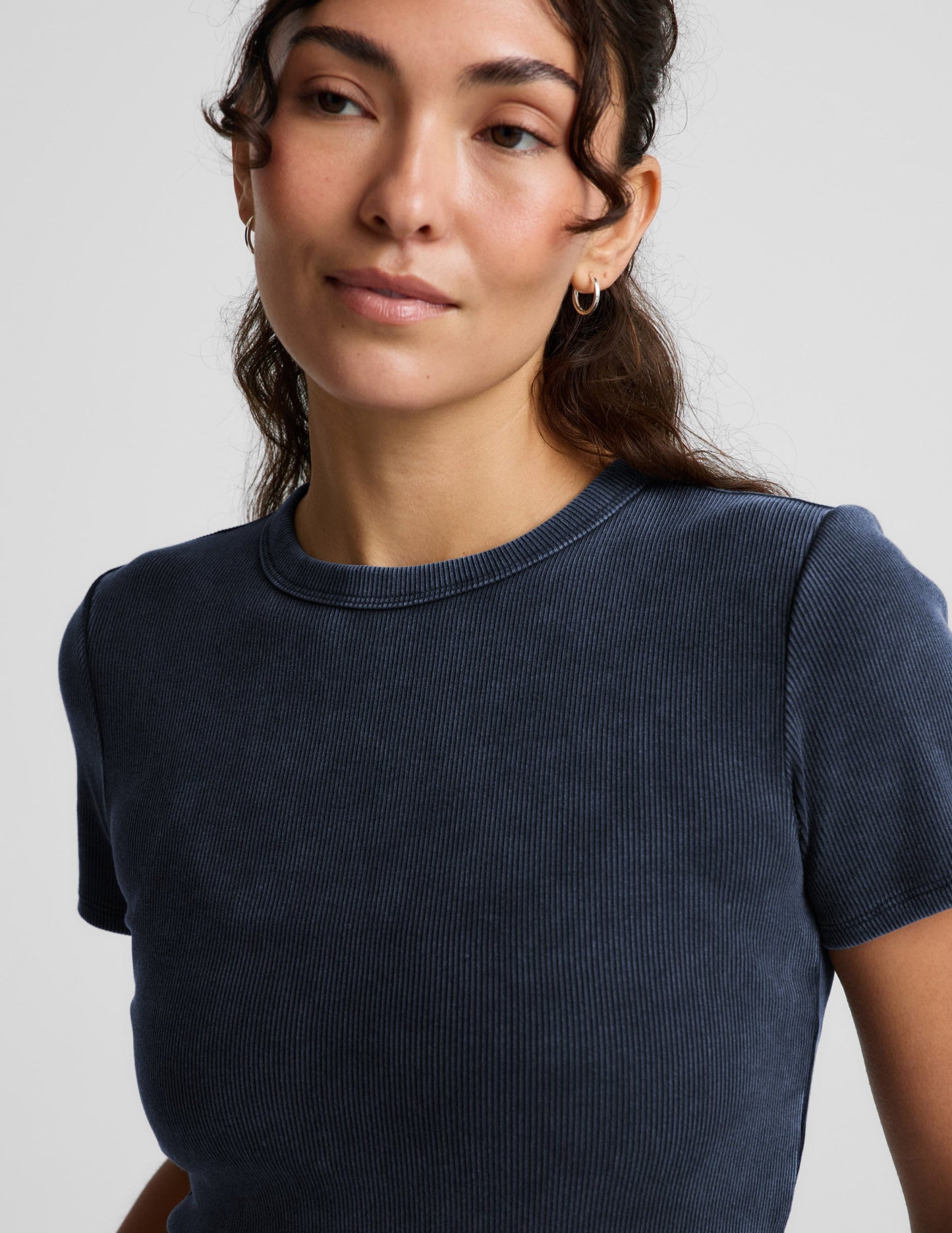 Woman wearing a navy blue ribbed t-shirt and white linen shorts against a plain background.