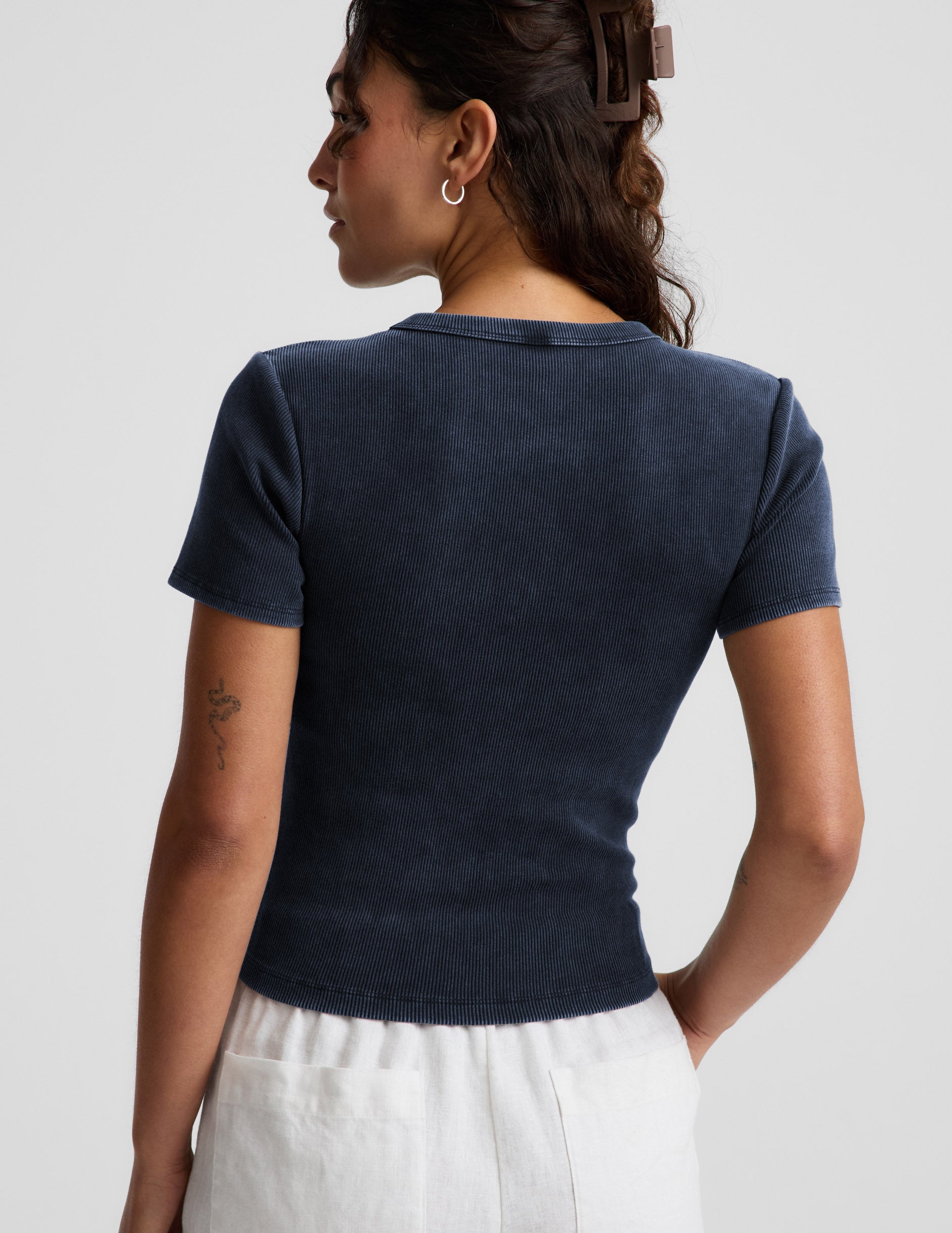 Woman wearing a navy blue ribbed t-shirt and white linen shorts against a plain background.