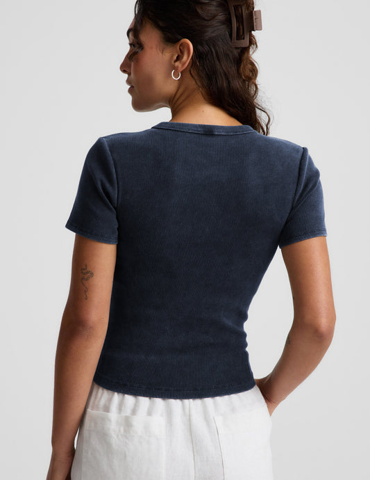 Woman wearing a navy blue ribbed t-shirt and white linen shorts against a plain background.