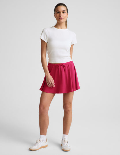 Woman wearing a white ribbed t-shirt and red skirt against a plain background.