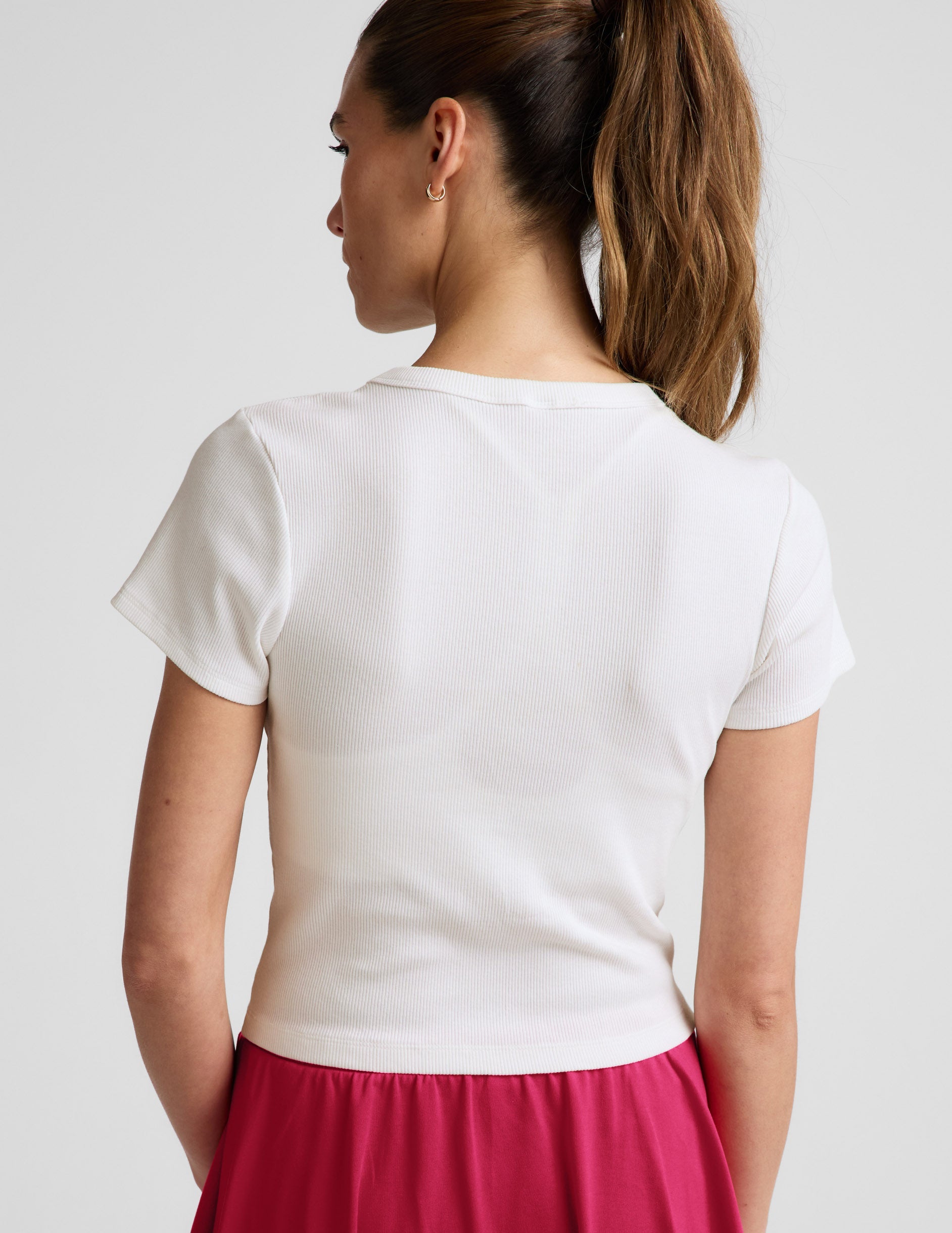 Woman wearing a white ribbed t-shirt and red skirt against a plain background.