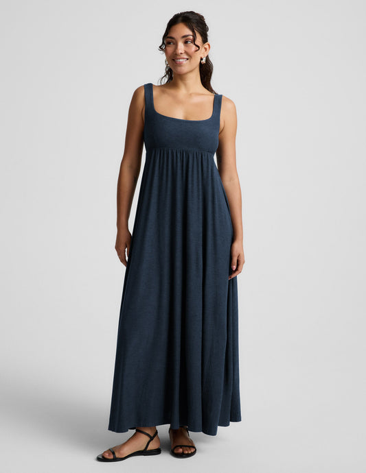 Woman wearing a navy blue sleeveless dress on a light gray background.