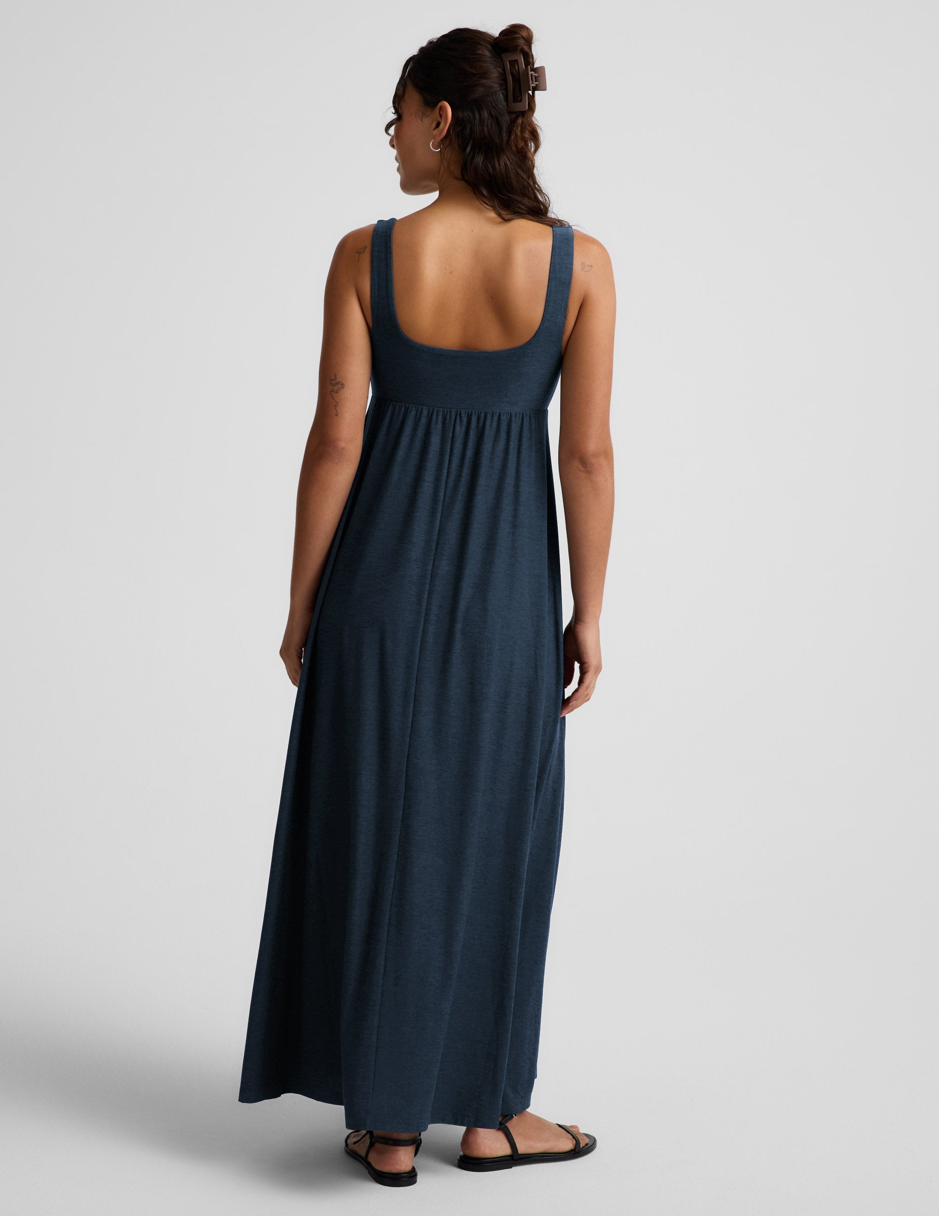 Woman wearing a navy blue sleeveless dress on a light gray background.