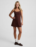 Woman wearing a brown mini tank dress against a light gray background.