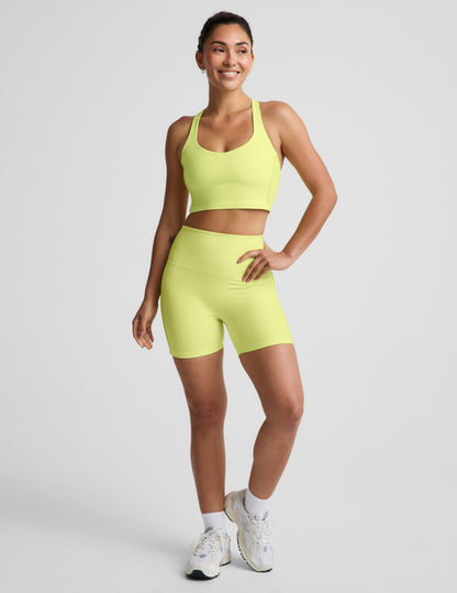 Woman wearing a bright yellow cropped tank and biker shorts against a plain background.