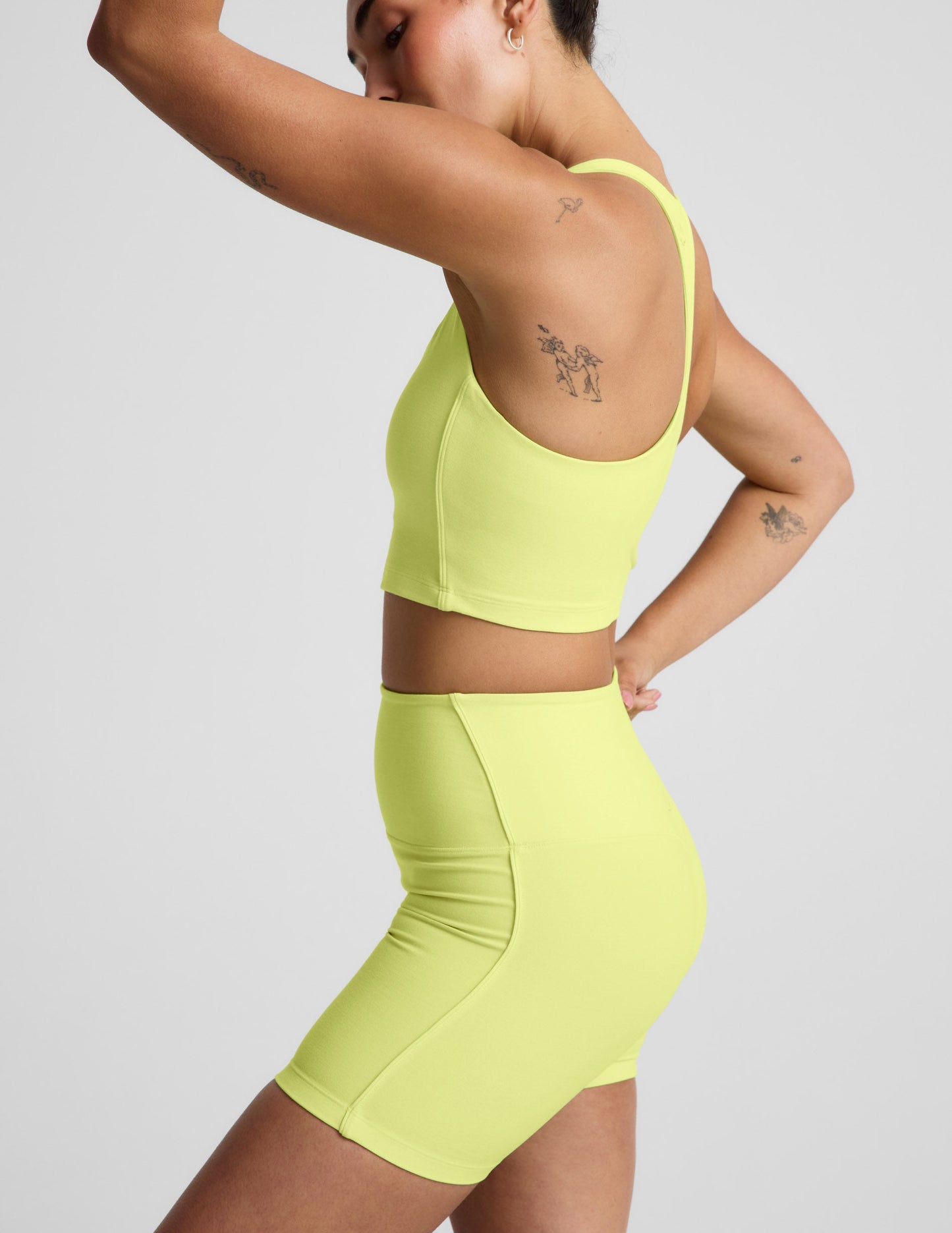 Woman wearing a bright yellow cropped tank and biker shorts against a plain background.