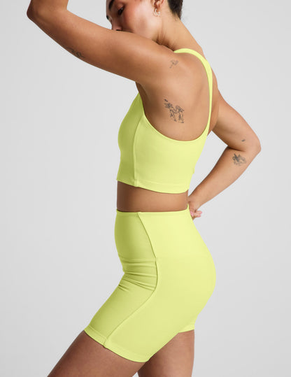 Woman wearing a bright yellow cropped tank and biker shorts against a plain background.