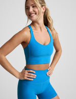 Woman wearing a blue racerback cropped tank and biker shorts against a plain background.