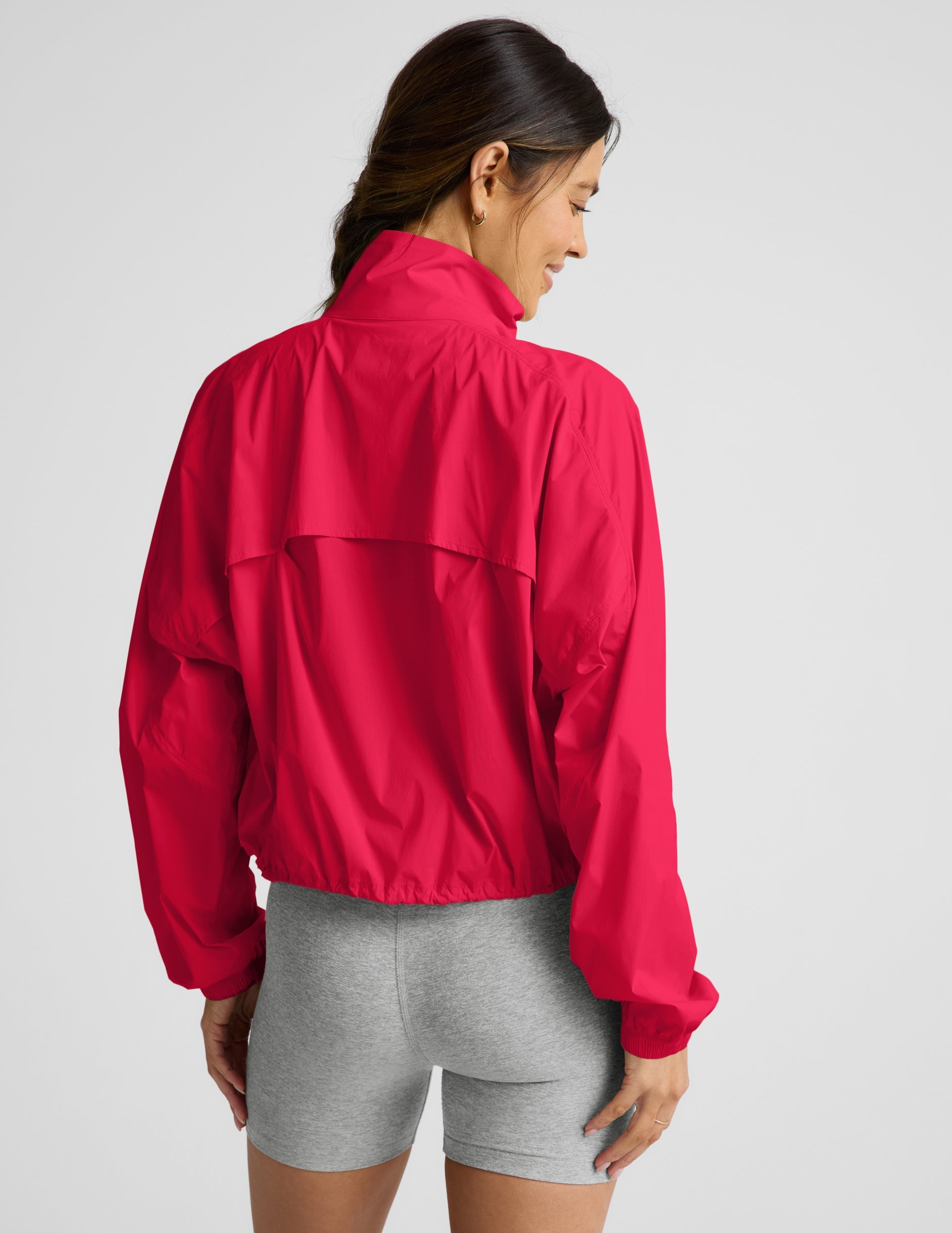 Woman wearing a bright red jacket and gray shorts on a light gray background.