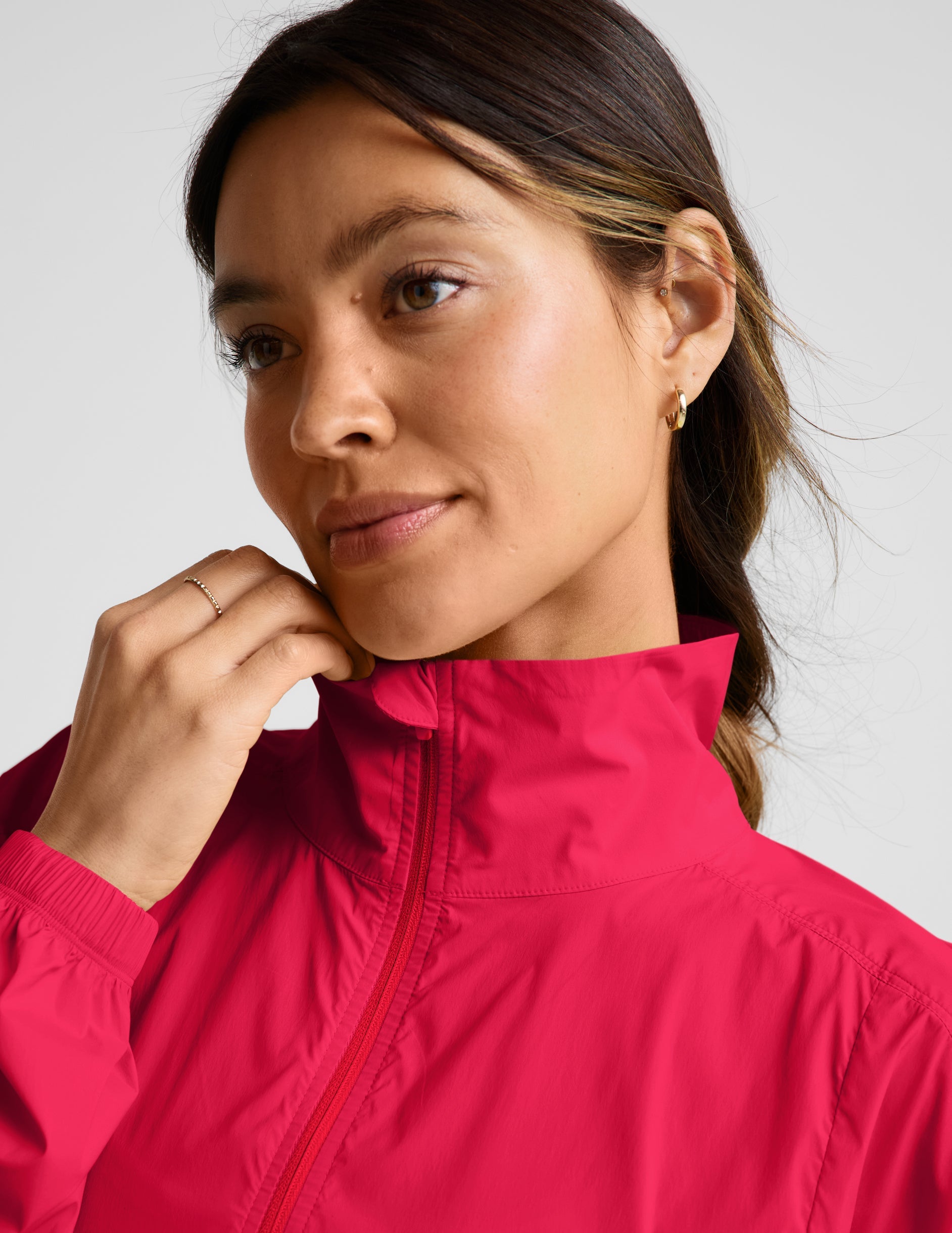 Woman wearing a bright red jacket and gray shorts on a light gray background.